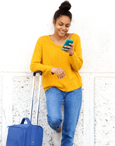 Woman smiling at her phone standing beside her luggage